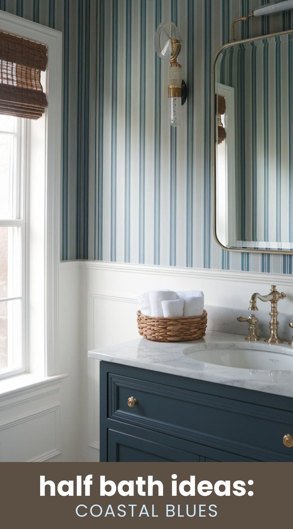 A stylish bathroom with blue and white vertical striped wallpaper, a navy blue vanity with a marble countertop, a brass faucet, and a wicker basket holding white towels. A window with a woven shade allows natural light in. Text reads half bath ideas: COASTAL BLUES.