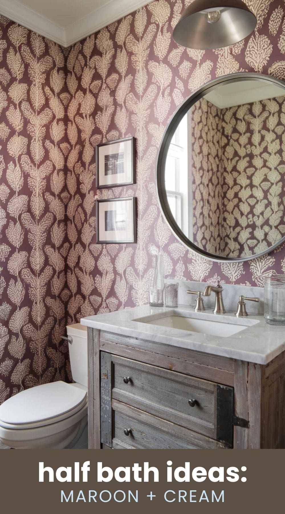 Cozy half bath with maroon and cream wallpaper featuring leaf patterns. A round mirror hangs above a rustic wooden vanity with a marble countertop. There is a silver sconce light above the mirror and two framed pictures on the wall.