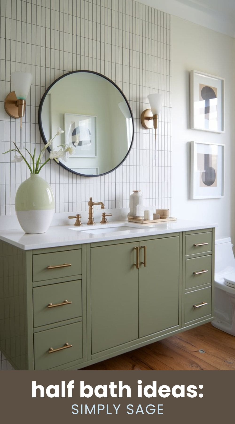 A modern bathroom features sage green cabinetry with gold handles, a white countertop, and a large round mirror. Two wall sconces provide soft lighting. The wall has a grid tile pattern, and there are framed prints and a vase with flowers.