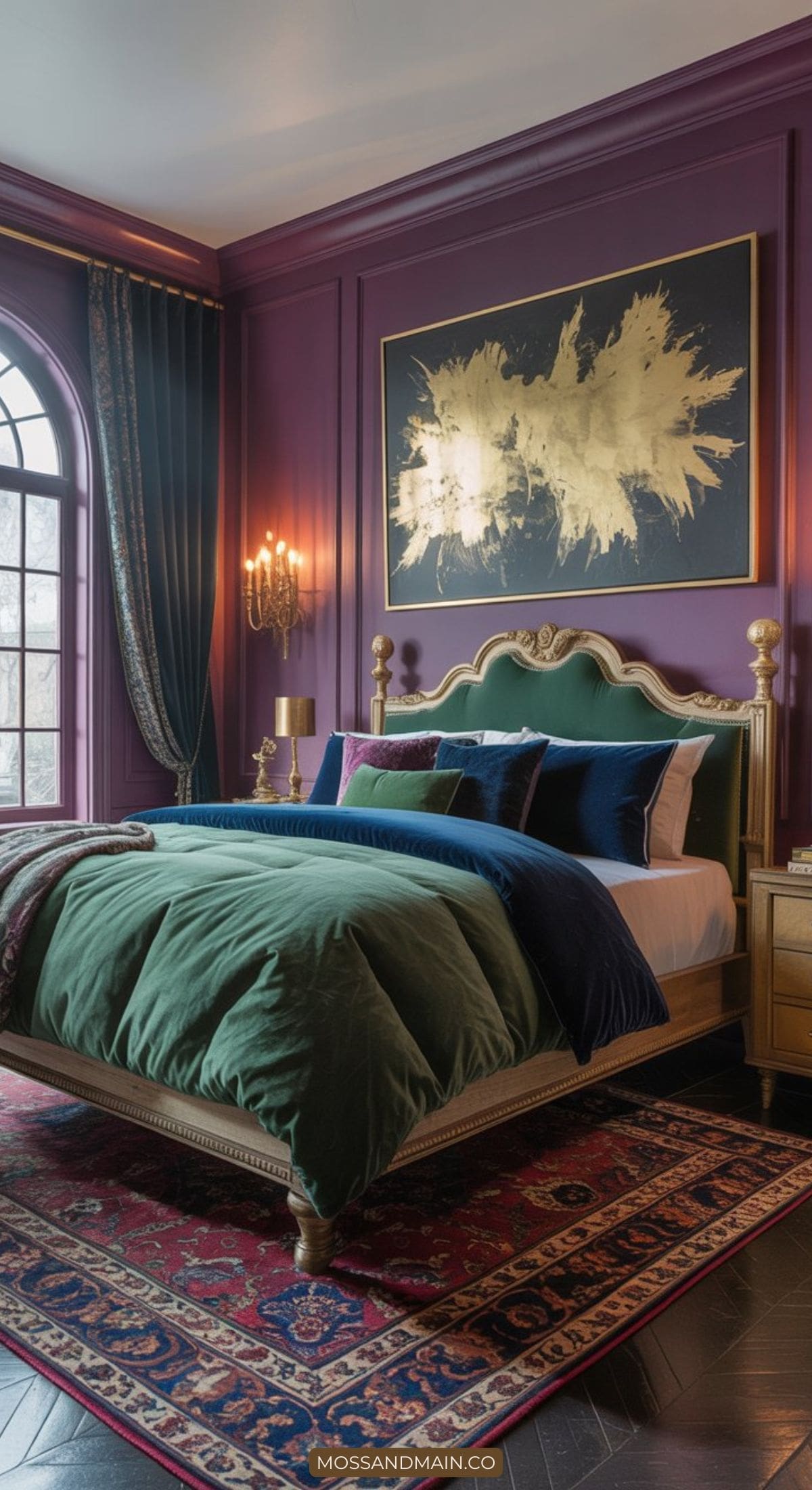 A luxurious bedroom features bold colors with a gold-trimmed bed, green and navy bedding, plush pillows, purple walls, a large gold abstract artwork, a red patterned rug, and an arched window with heavy drapes.