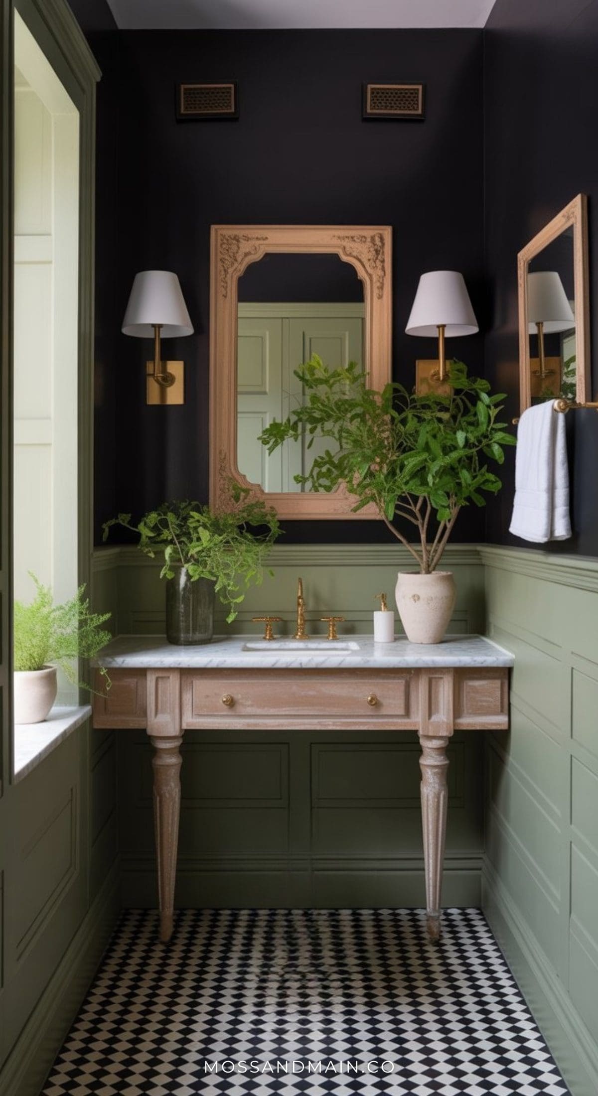 Chic dark green bathroom with paneled walls, black upper walls, marble sink, brass fixtures, large gold-framed mirror, two wall sconces, potted plants, and black-and-white checkered floor tiles.