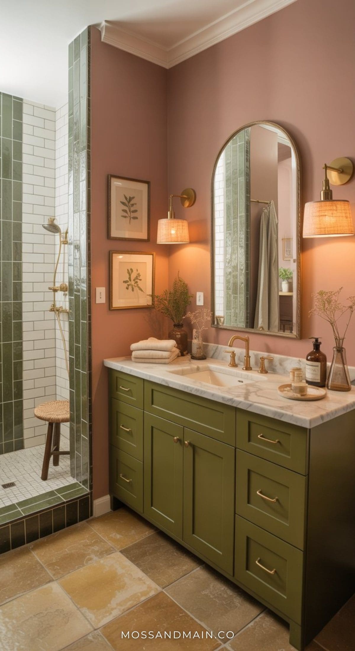 A stylish pink bathroom featuring bold pink walls, a green vanity with marble countertop, brass fixtures, two arched mirrors, wall sconces, botanical art, and a walk-in shower with green subway tiles and a wooden stool.