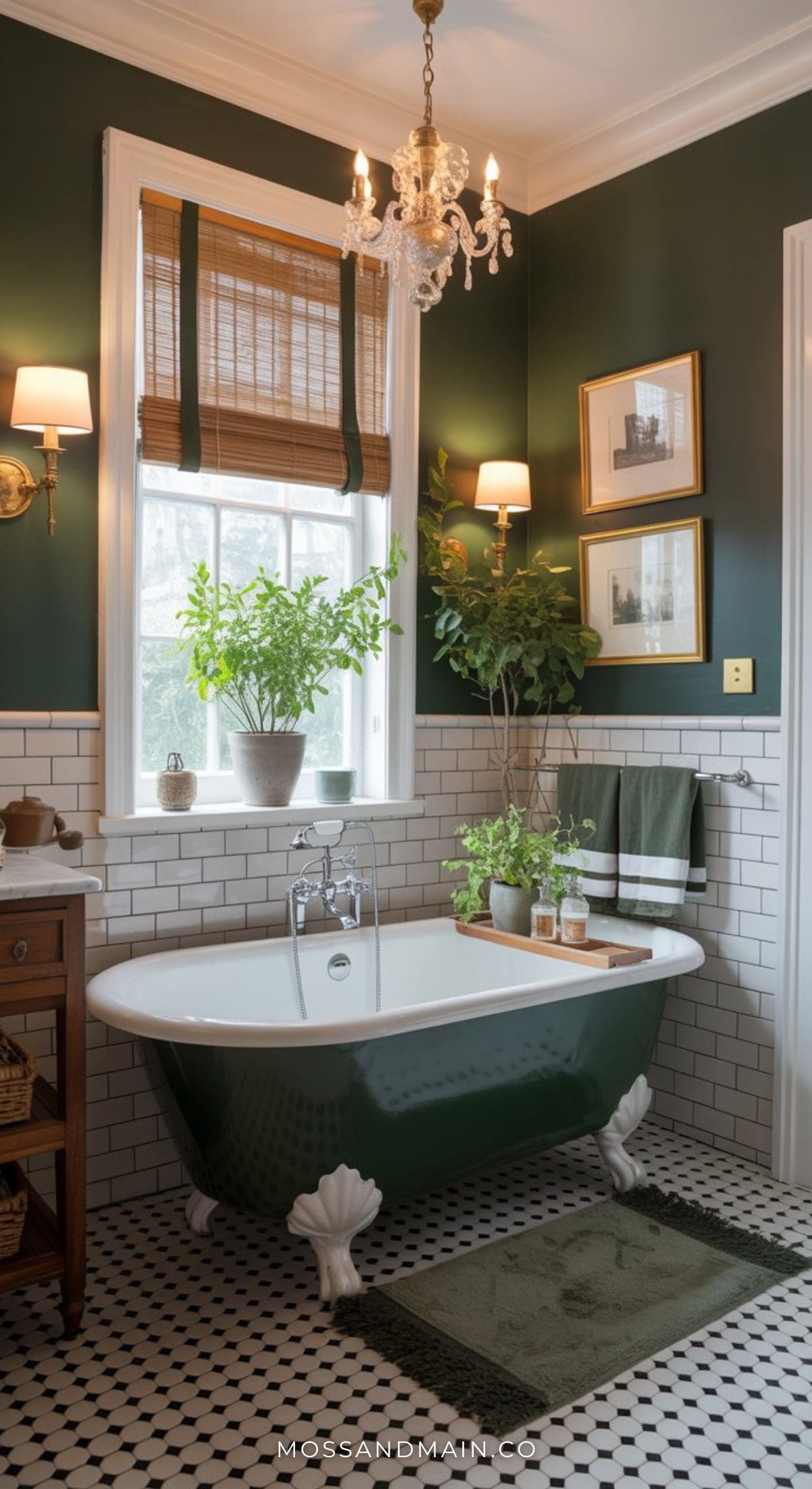 A luxe, moody bathroom with dark green walls features a clawfoot tub, white subway tiles, black-and-white floor tiles, leafy plants, framed artwork, and a chandelier. Natural light streams in through the window.