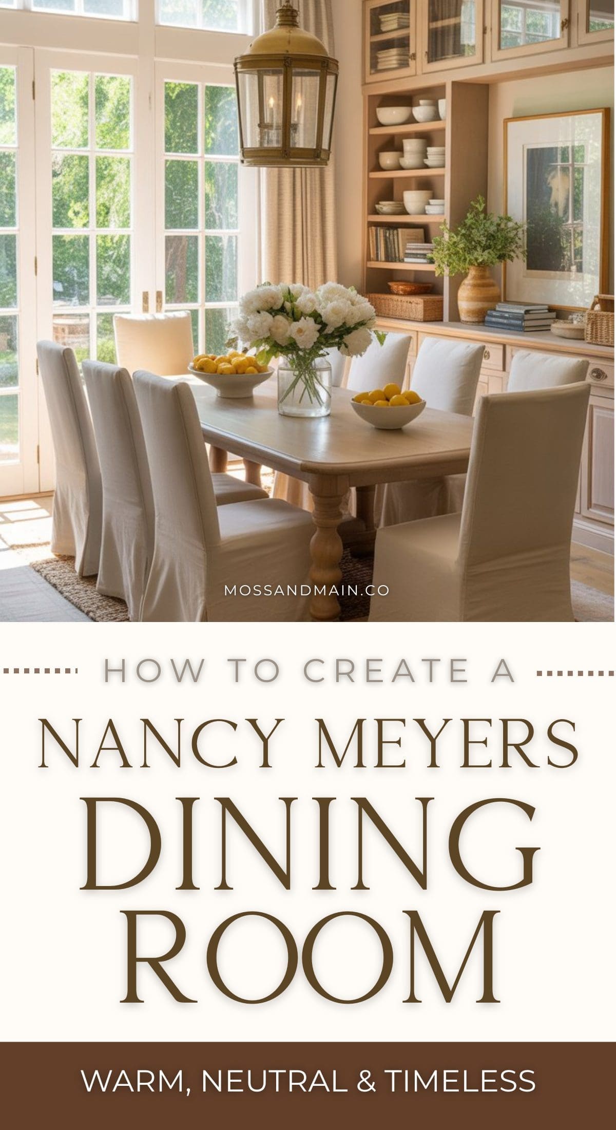 A bright, elegant Nancy Meyers dining room with a wooden table, white upholstered chairs, large windows, and built-in shelves; decorated with flowers and lemons for a warm, neutral dining room style. Text: “How to create a Nancy Meyers dining room.”.