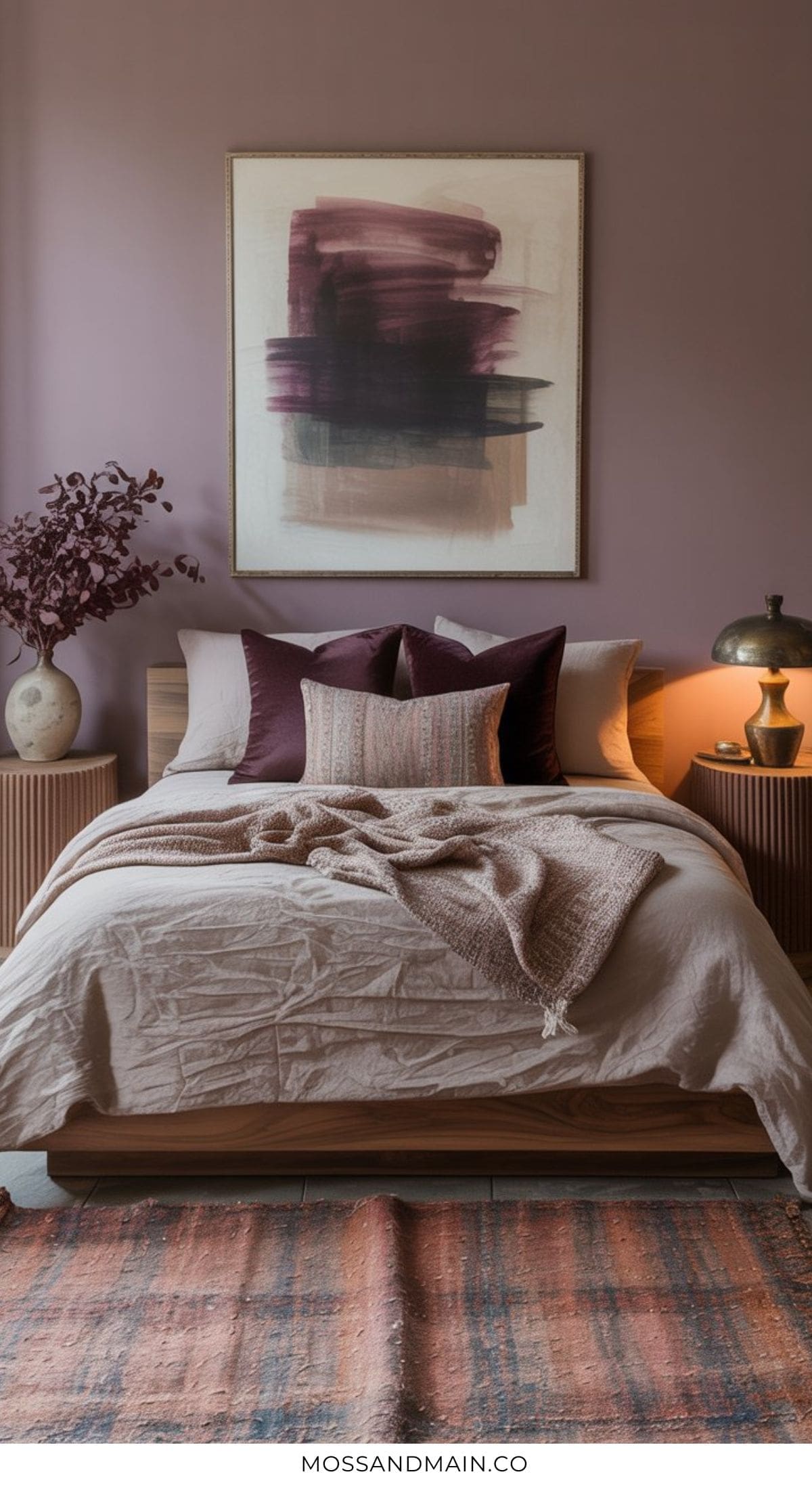 A cozy bedroom with a soft beige bedspread, mauve and burgundy pillows, taupe knit throw, abstract wall art, and warm lighting offers perfect inspiration for cozy bedroom ideas and inviting warm bedroom decor.