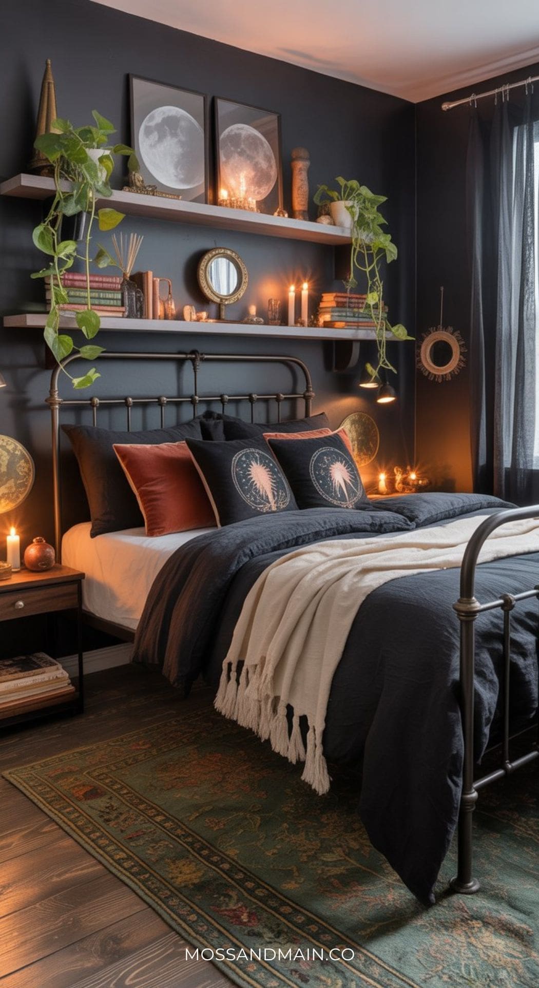 Cozy black boho bedroom with dark walls, metal bed frame, moon-themed art, shelves of plants and candles, layered bedding in black and cream, velvet pillows, a tasseled throw, patterned rug on wood floor, and warm ambient lighting.